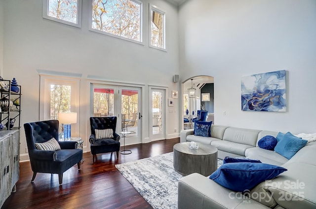 living room featuring plenty of natural light, a towering ceiling, arched walkways, and dark wood-type flooring