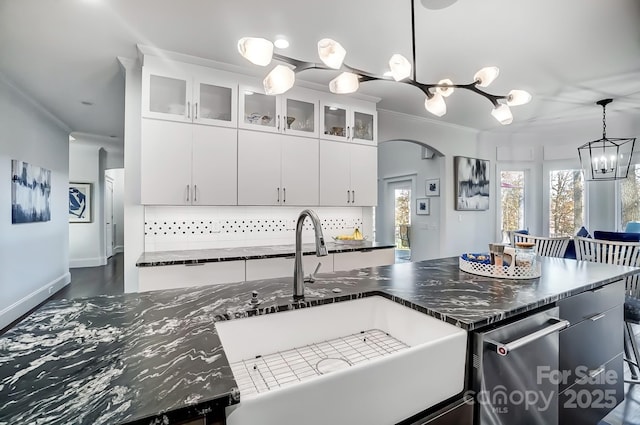 kitchen with ornamental molding, a sink, decorative light fixtures, glass insert cabinets, and white cabinetry