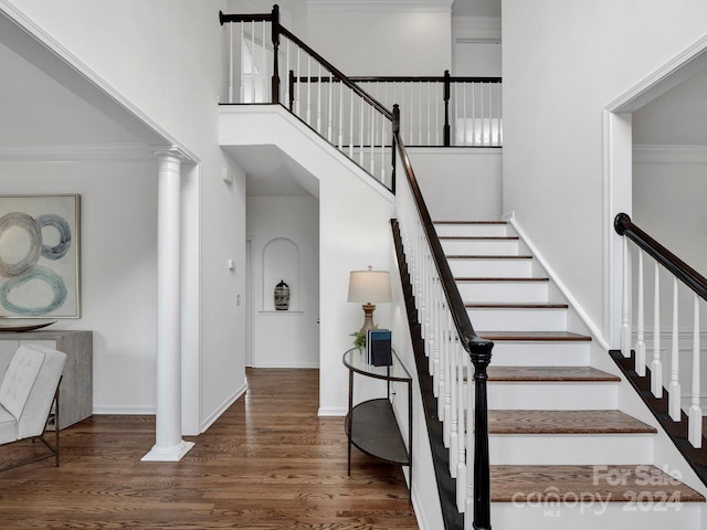 stairway with hardwood / wood-style floors, a towering ceiling, ornate columns, and ornamental molding