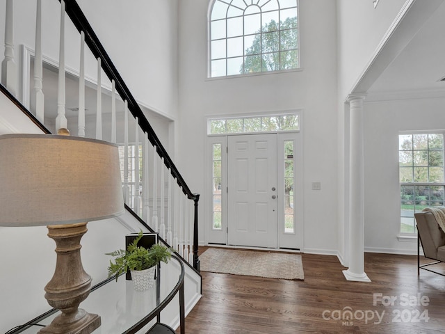 foyer with a towering ceiling, dark hardwood / wood-style floors, plenty of natural light, and decorative columns