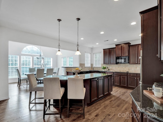 kitchen featuring tasteful backsplash, a kitchen island, dark brown cabinetry, dark hardwood / wood-style floors, and hanging light fixtures