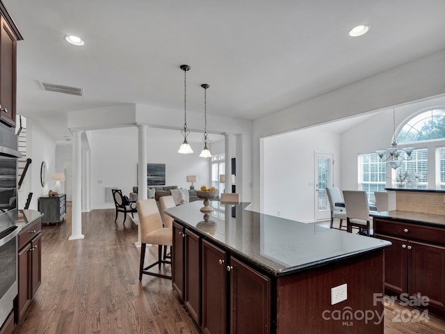 kitchen with dark hardwood / wood-style flooring, a notable chandelier, decorative columns, a kitchen island, and a breakfast bar