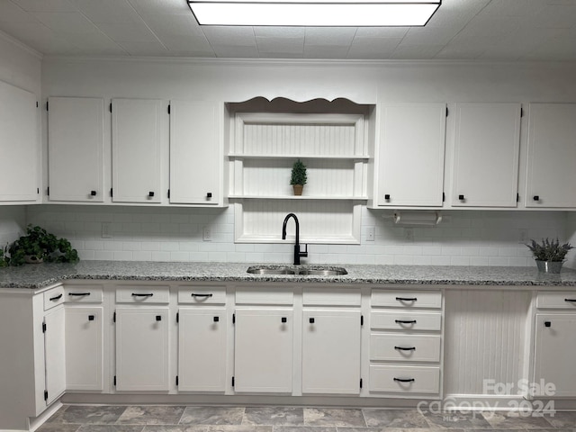 kitchen featuring white cabinetry, light stone counters, ornamental molding, and sink