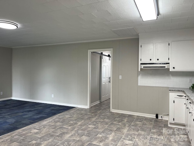 interior space featuring white cabinetry, light stone countertops, a barn door, crown molding, and decorative backsplash