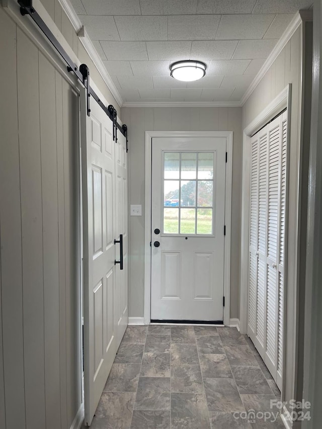 doorway to outside featuring wooden walls, ornamental molding, and a barn door