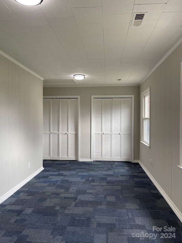 unfurnished bedroom with wooden walls, two closets, dark carpet, and crown molding