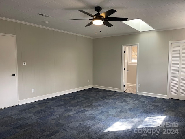 spare room featuring a skylight, ceiling fan, dark colored carpet, and ornamental molding