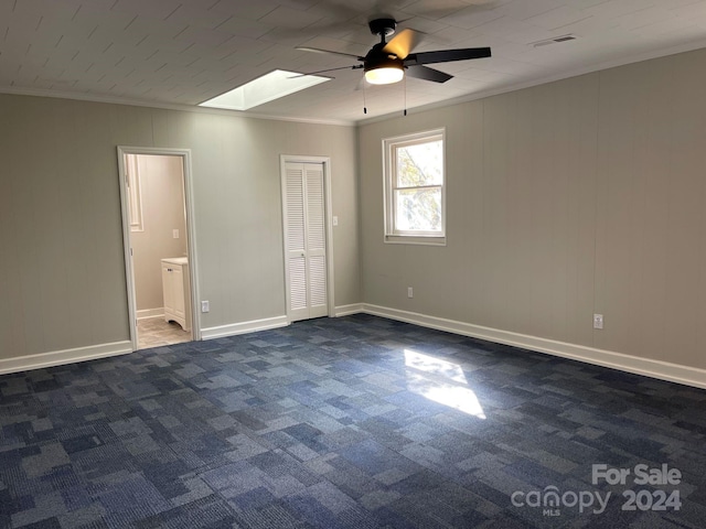 carpeted empty room with a skylight, ceiling fan, and crown molding