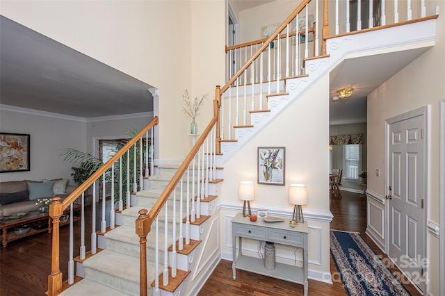 stairway with a high ceiling, hardwood / wood-style flooring, ornate columns, and ornamental molding