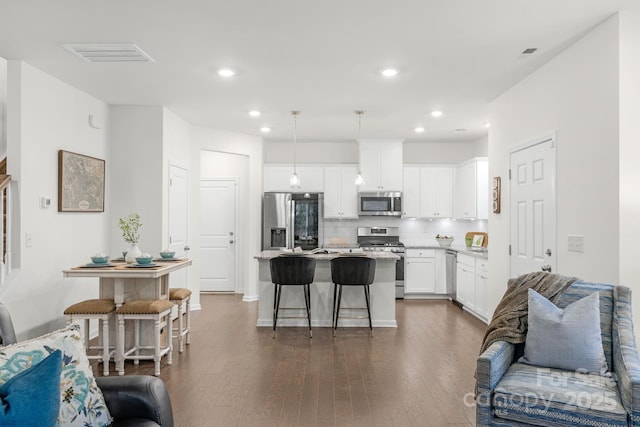 kitchen with a center island, a kitchen breakfast bar, appliances with stainless steel finishes, decorative light fixtures, and white cabinetry