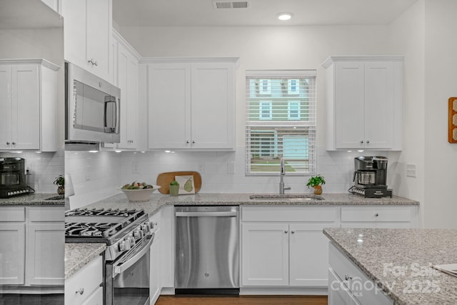 kitchen with sink, decorative backsplash, light stone counters, white cabinetry, and stainless steel appliances