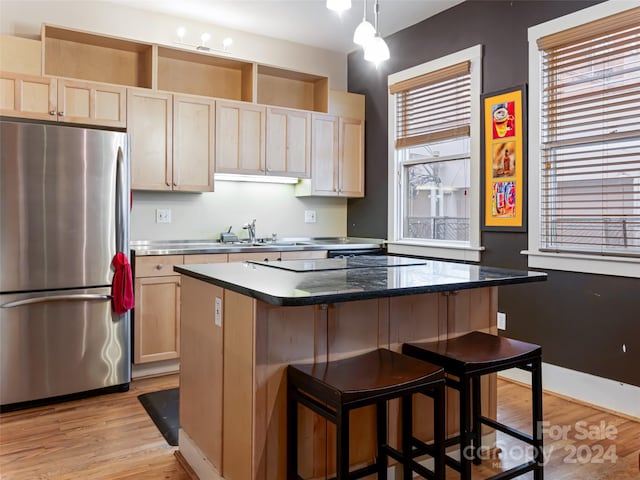 kitchen with light wood-type flooring, hanging light fixtures, stainless steel refrigerator, and a center island