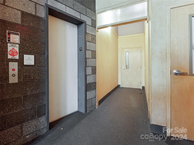 hallway featuring elevator, crown molding, and dark carpet