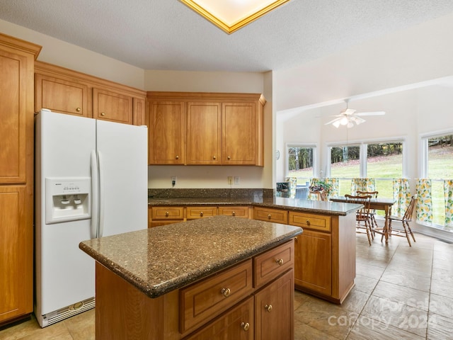 kitchen with a textured ceiling, white fridge with ice dispenser, ceiling fan, a kitchen island, and dark stone countertops