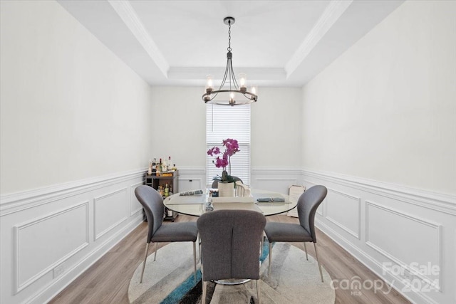 dining space with crown molding, light hardwood / wood-style floors, a notable chandelier, and a raised ceiling