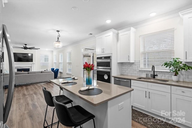 kitchen featuring a kitchen bar, sink, white cabinetry, appliances with stainless steel finishes, and decorative light fixtures