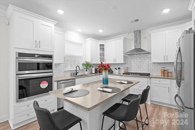 kitchen with white cabinetry, appliances with stainless steel finishes, wall chimney exhaust hood, and a breakfast bar area