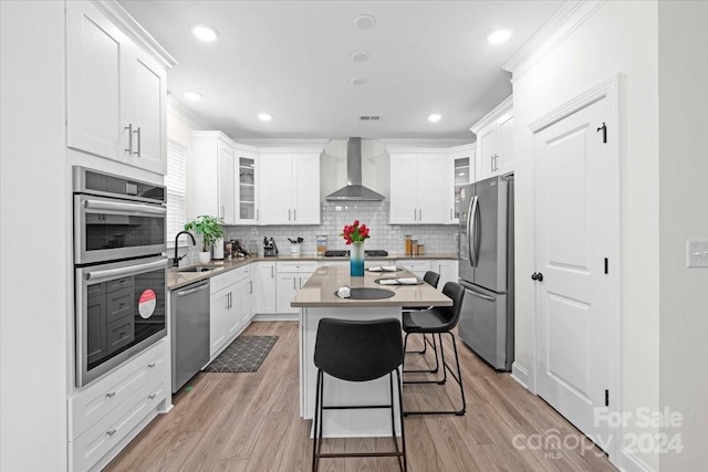 kitchen featuring stainless steel appliances, wall chimney range hood, white cabinets, and a center island