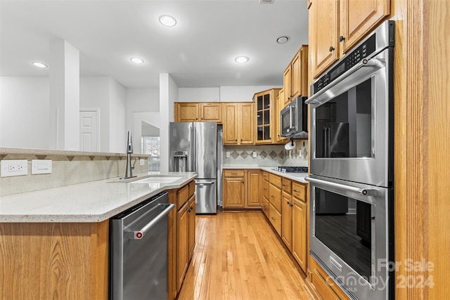 kitchen with sink, decorative backsplash, light stone countertops, light wood-type flooring, and appliances with stainless steel finishes