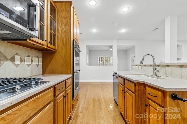 kitchen with sink, decorative backsplash, ceiling fan, light wood-type flooring, and appliances with stainless steel finishes