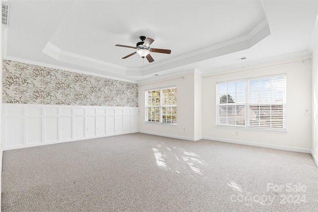 carpeted empty room with a raised ceiling, ceiling fan, plenty of natural light, and crown molding