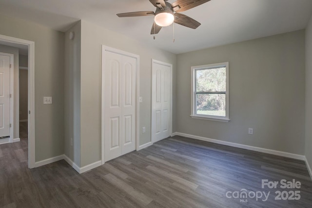 unfurnished bedroom with a ceiling fan, dark wood-style floors, multiple closets, and baseboards