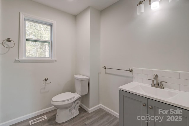 half bathroom with visible vents, toilet, decorative backsplash, wood finished floors, and vanity