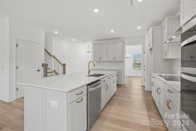 kitchen featuring white cabinetry, sink, appliances with stainless steel finishes, an island with sink, and light wood-type flooring