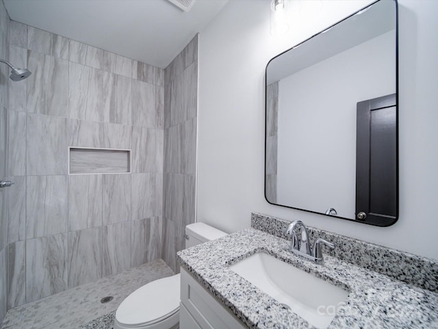 bathroom featuring toilet, vanity, and a tile shower