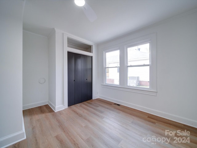 unfurnished bedroom featuring light hardwood / wood-style flooring, ceiling fan, crown molding, and a closet