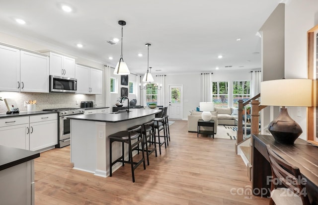 kitchen featuring white cabinets, stainless steel appliances, decorative light fixtures, and light hardwood / wood-style flooring