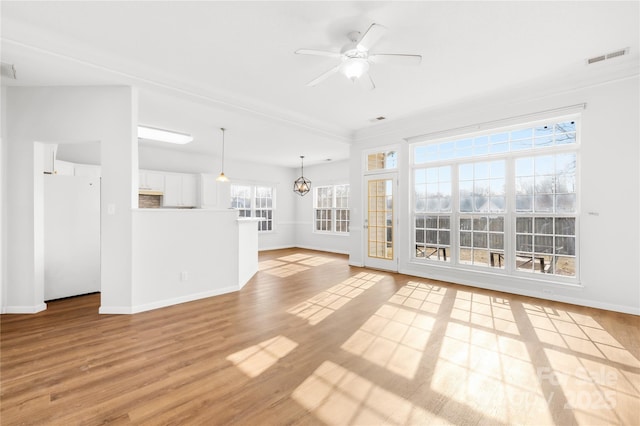 unfurnished living room with ceiling fan with notable chandelier and light hardwood / wood-style floors