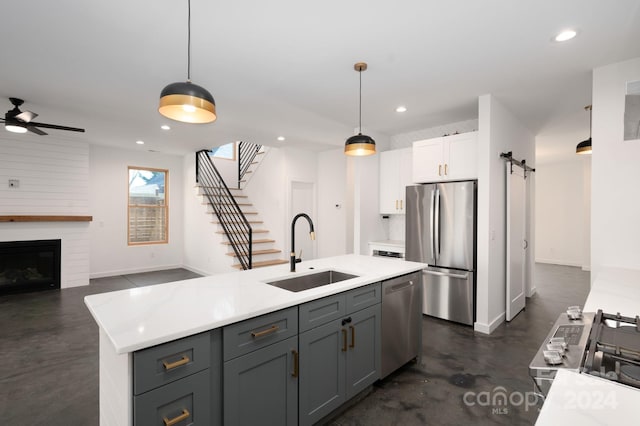 kitchen featuring stainless steel appliances, a barn door, hanging light fixtures, sink, and white cabinets