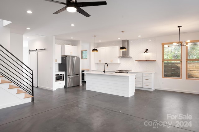 kitchen featuring white cabinets, appliances with stainless steel finishes, wall chimney exhaust hood, and a barn door