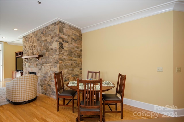 dining space with a stone fireplace, light hardwood / wood-style flooring, and crown molding