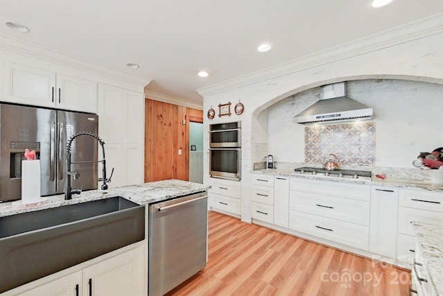 kitchen with white cabinets, wall chimney exhaust hood, stainless steel appliances, sink, and backsplash