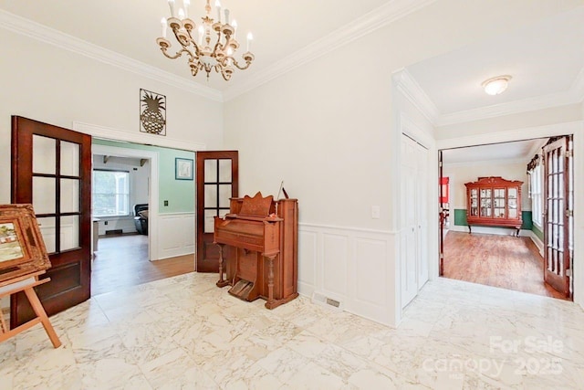 hallway featuring an inviting chandelier, crown molding, and french doors