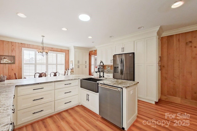 kitchen with wood walls, stainless steel appliances, hanging light fixtures, ornamental molding, and light stone counters