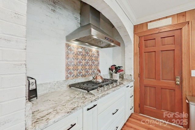 kitchen featuring white cabinetry, ventilation hood, stainless steel gas cooktop, light stone counters, and crown molding