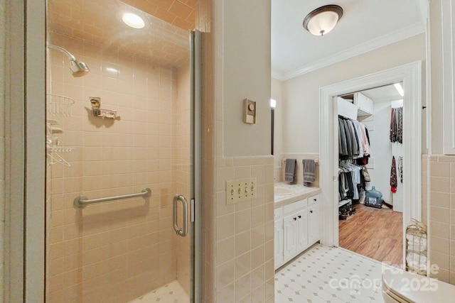 bathroom with a shower with shower door, vanity, tile walls, and ornamental molding