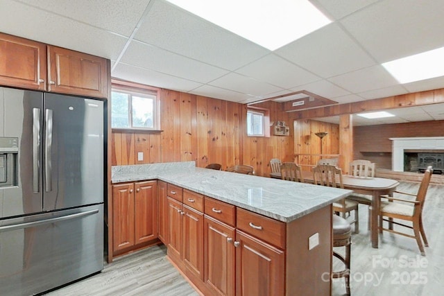 kitchen with stainless steel refrigerator with ice dispenser, kitchen peninsula, a drop ceiling, and a breakfast bar