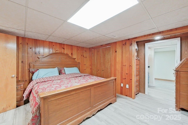 bedroom featuring a paneled ceiling, light hardwood / wood-style floors, and wood walls