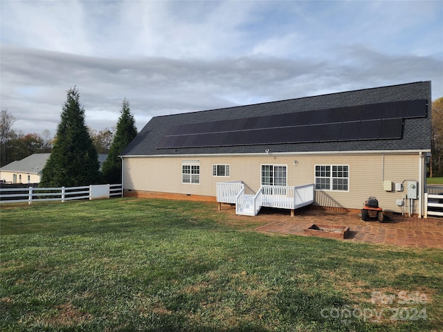 rear view of property with solar panels, a lawn, and a deck