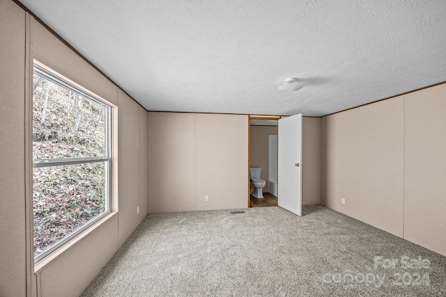 unfurnished bedroom featuring ensuite bathroom, multiple windows, and a textured ceiling