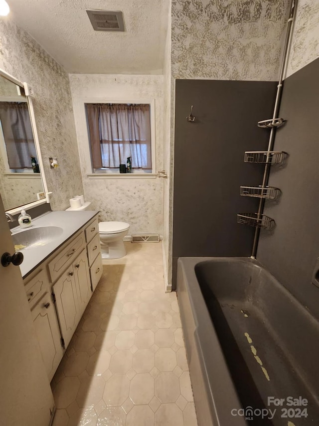 bathroom with a textured ceiling, vanity, tile patterned floors, toilet, and a bathtub