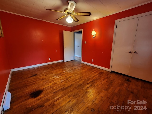 unfurnished bedroom with wood-type flooring, ornamental molding, baseboard heating, ceiling fan, and a closet