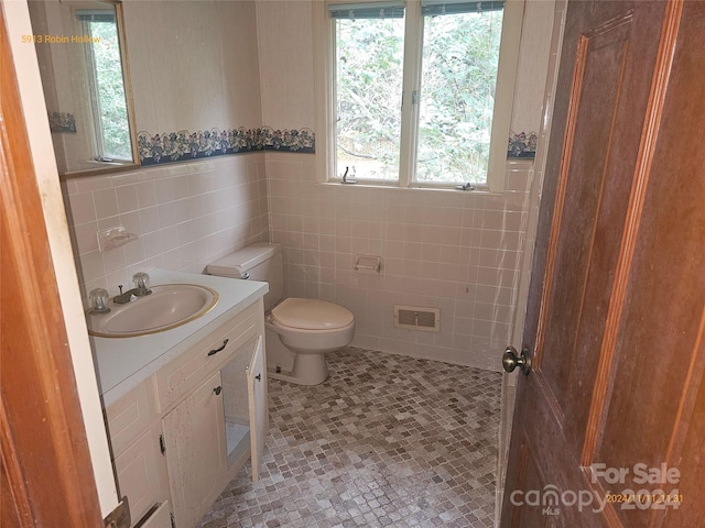 bathroom featuring toilet, vanity, tile walls, and tile patterned flooring