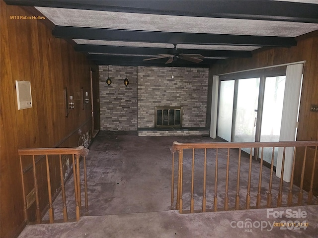 unfurnished living room with a brick fireplace, wood walls, beamed ceiling, and ceiling fan