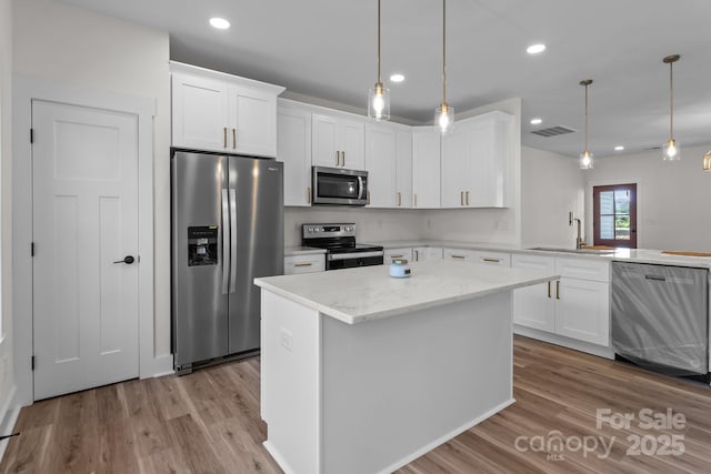 kitchen featuring sink, a kitchen island, decorative light fixtures, stainless steel appliances, and white cabinets