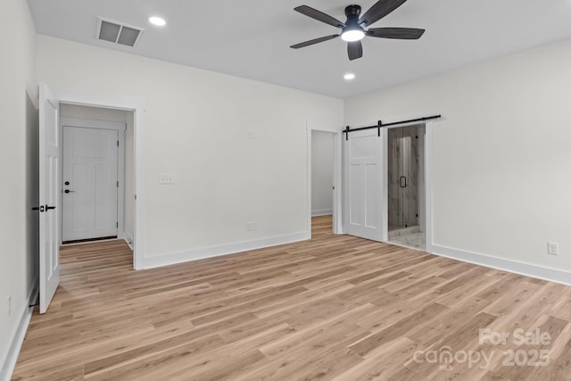 unfurnished bedroom featuring ceiling fan, connected bathroom, light hardwood / wood-style floors, and a barn door